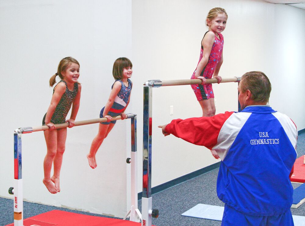 Young gymnasts on the bars with a coach spotting